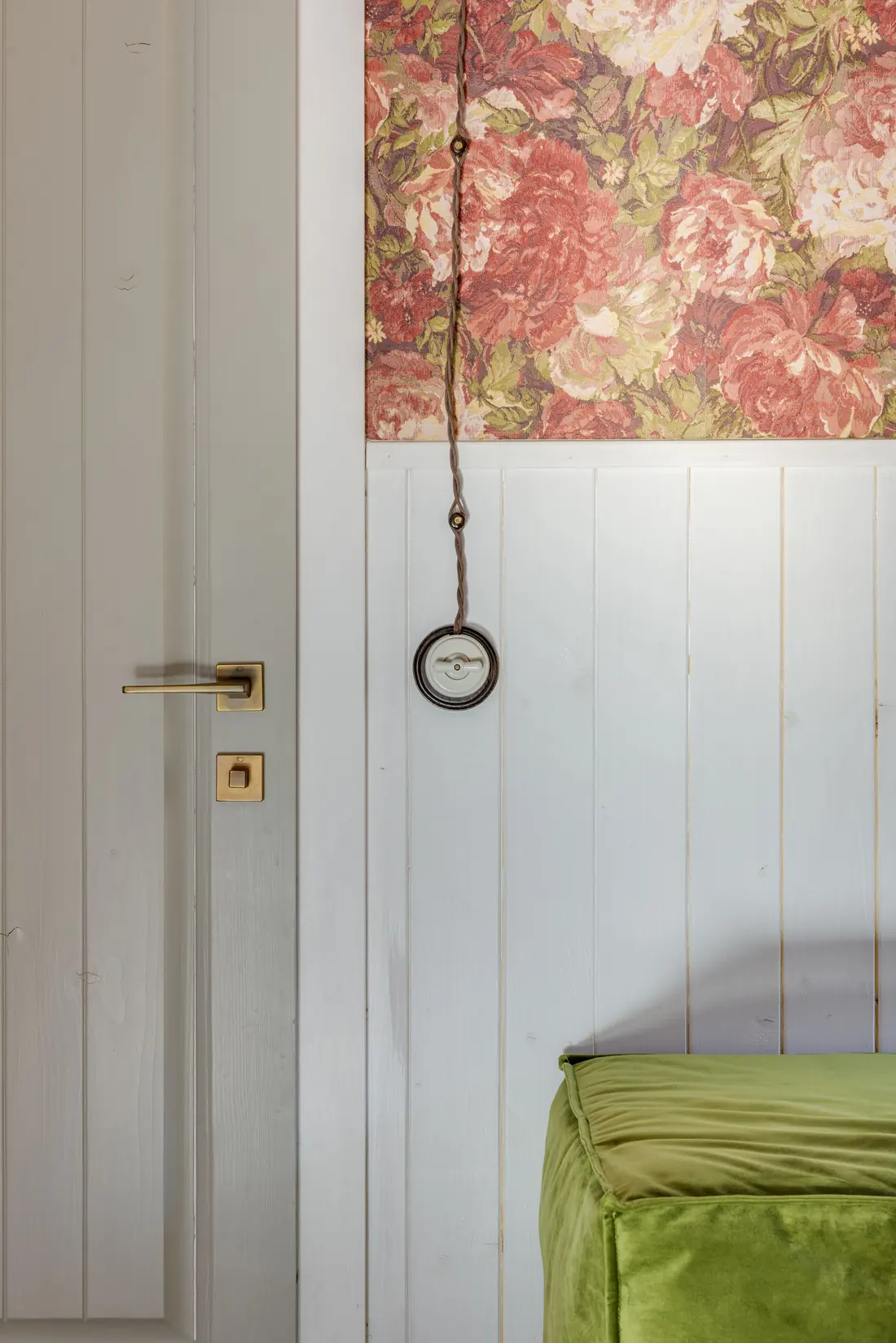 Close-up of a feature wall showing a change from floral wallpaper above to painted wainscoting below, with a brass door handle