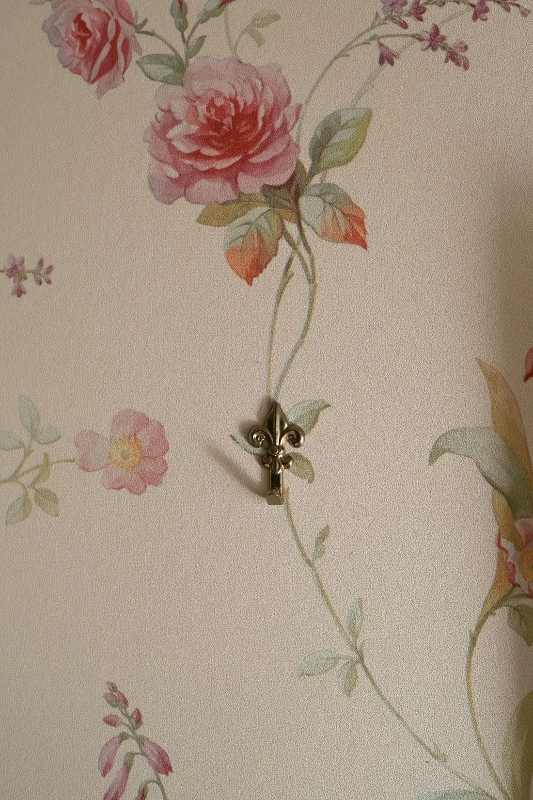 Close-up detail of a delicate rose wallpaper pattern with a small brass fleur-de-lis hook