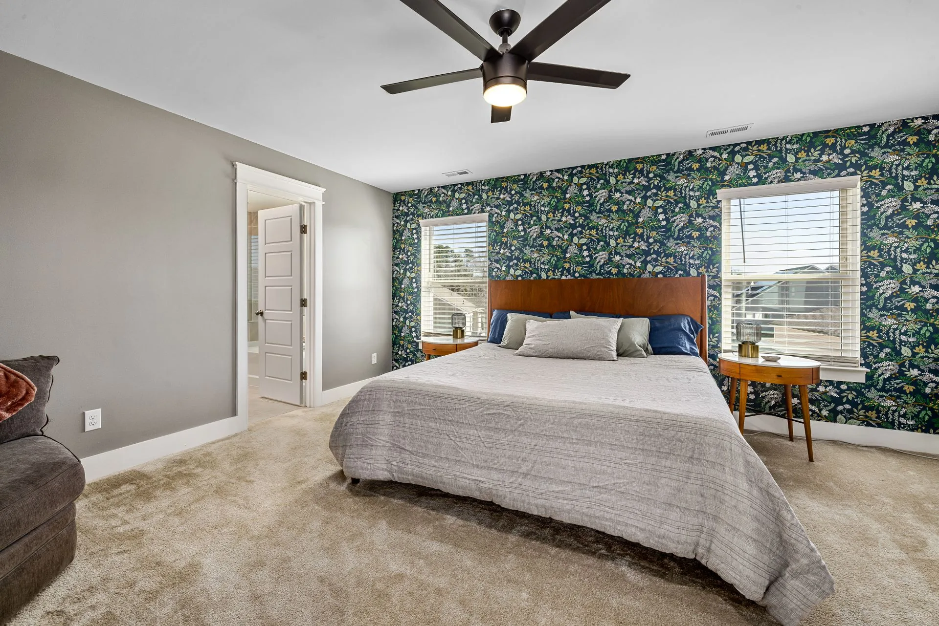 Bright primary bedroom with a bold navy botanical-print wallpaper accent wall, wood headboard, and soft natural light